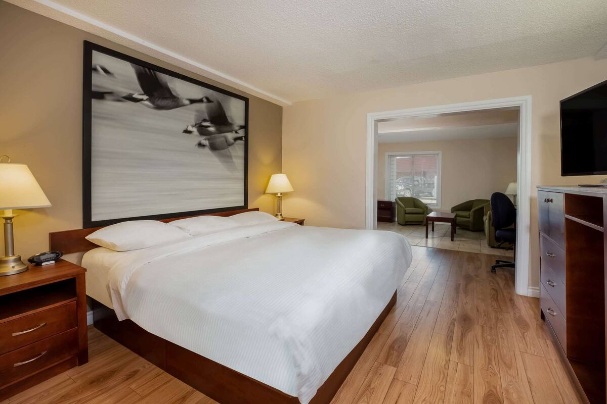A hotel room with a large bed, bedside lamps, a flat-screen TV, a wooden dresser, and a framed picture on the wall.