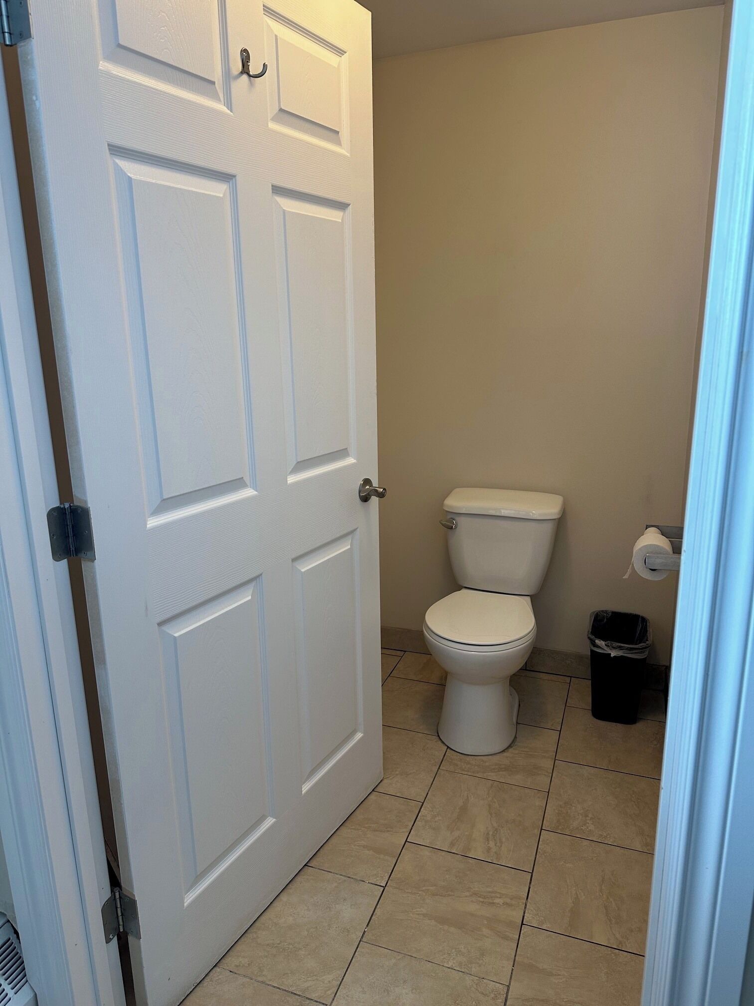 A small bathroom with a white toilet, a trash bin, and a door.