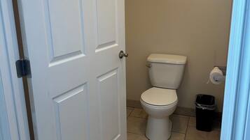 A small bathroom with a white toilet, a trash bin, and a door.