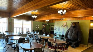 Un restaurante con techos de madera, varias mesas y sillas, y una estatua de un oso en la pared.