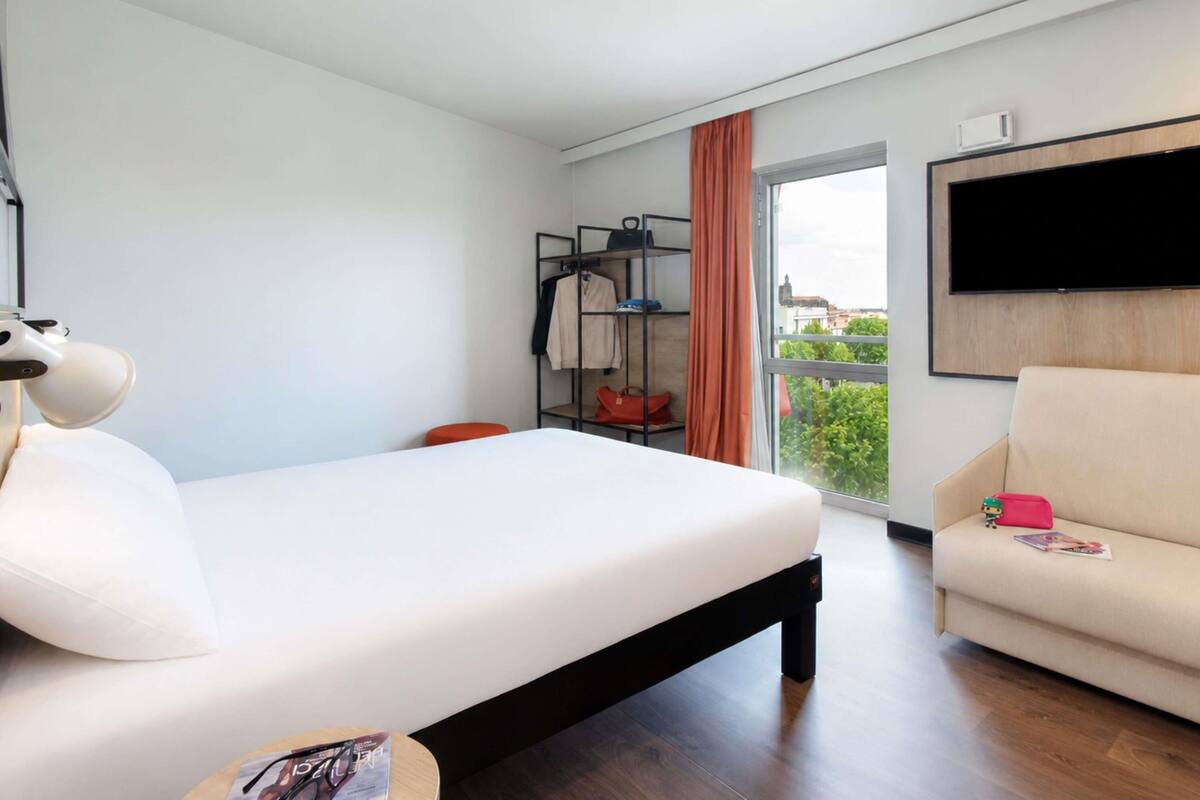 Quarto de hotel moderno com cama, sofá, televisão e janela com vista.