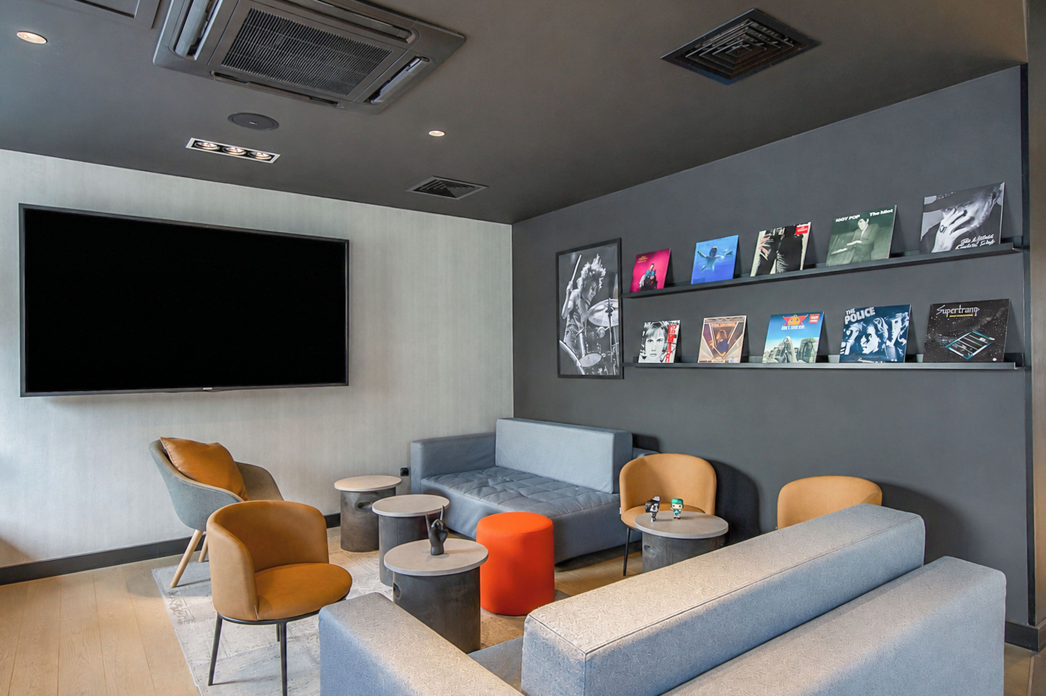 Un área de descanso moderna con asientos, un televisor de pantalla plana y una pared decorada con obras enmarcadas.