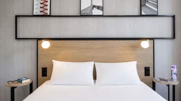 Une chambre d’hôtel comprenant un lit, deux tables de chevet, une étagère avec des photos encadrées et une tête de lit en bois.