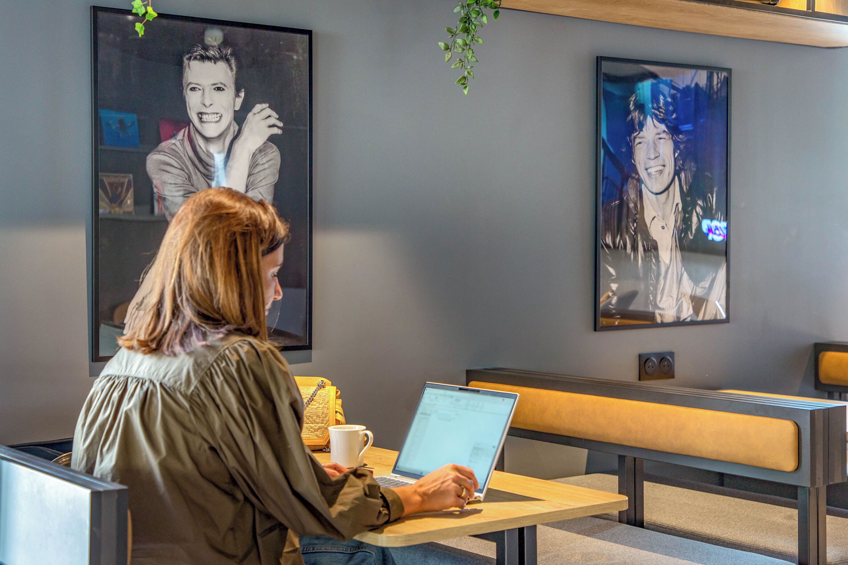 Une personne utilise un ordinateur portable à une table, près d’un banc, dans une pièce dont les murs sont ornés d’œuvres d’art.
