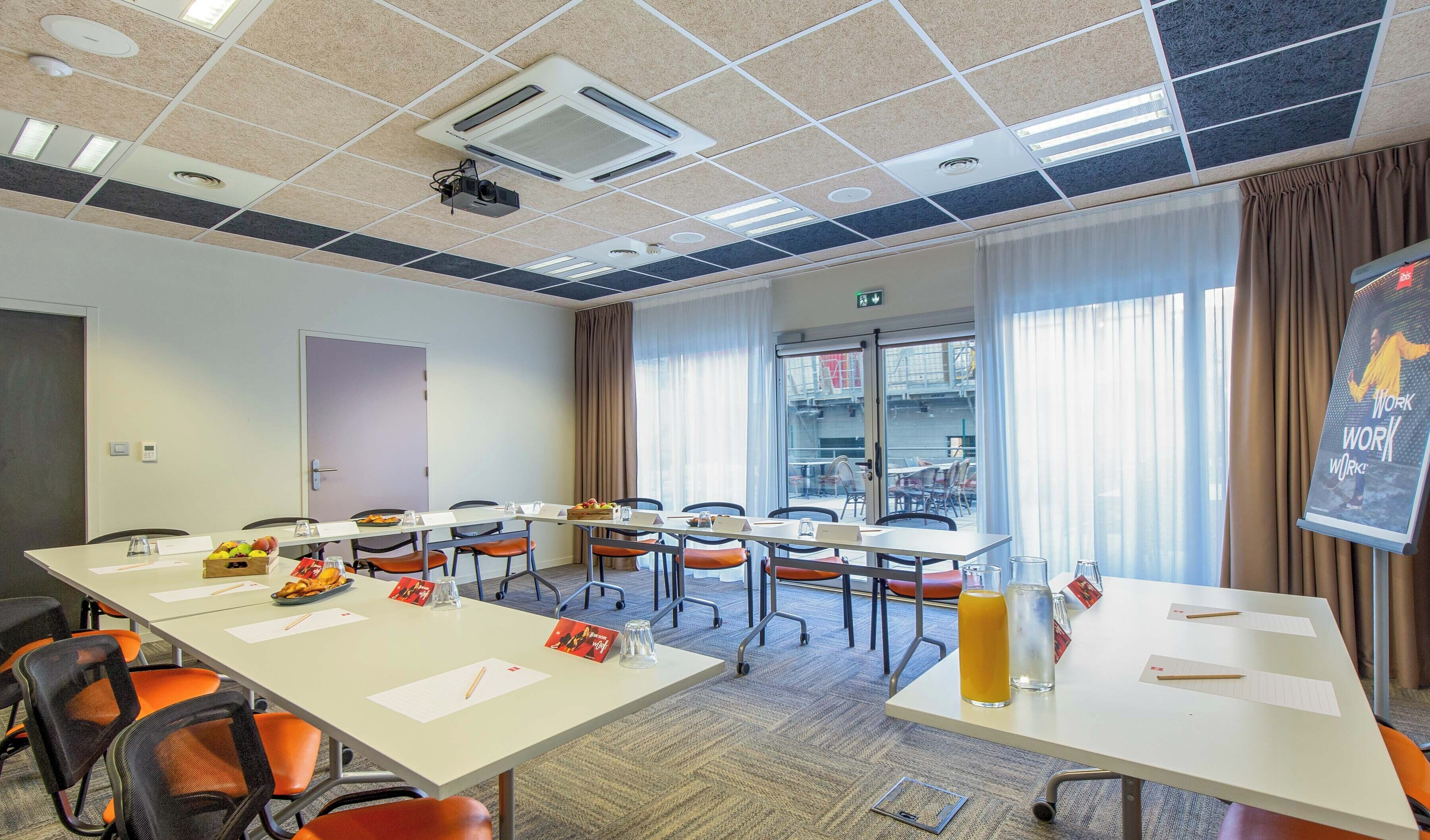 A conference room with a projector, a large table with chairs, a window with curtains, and a poster on the wall.