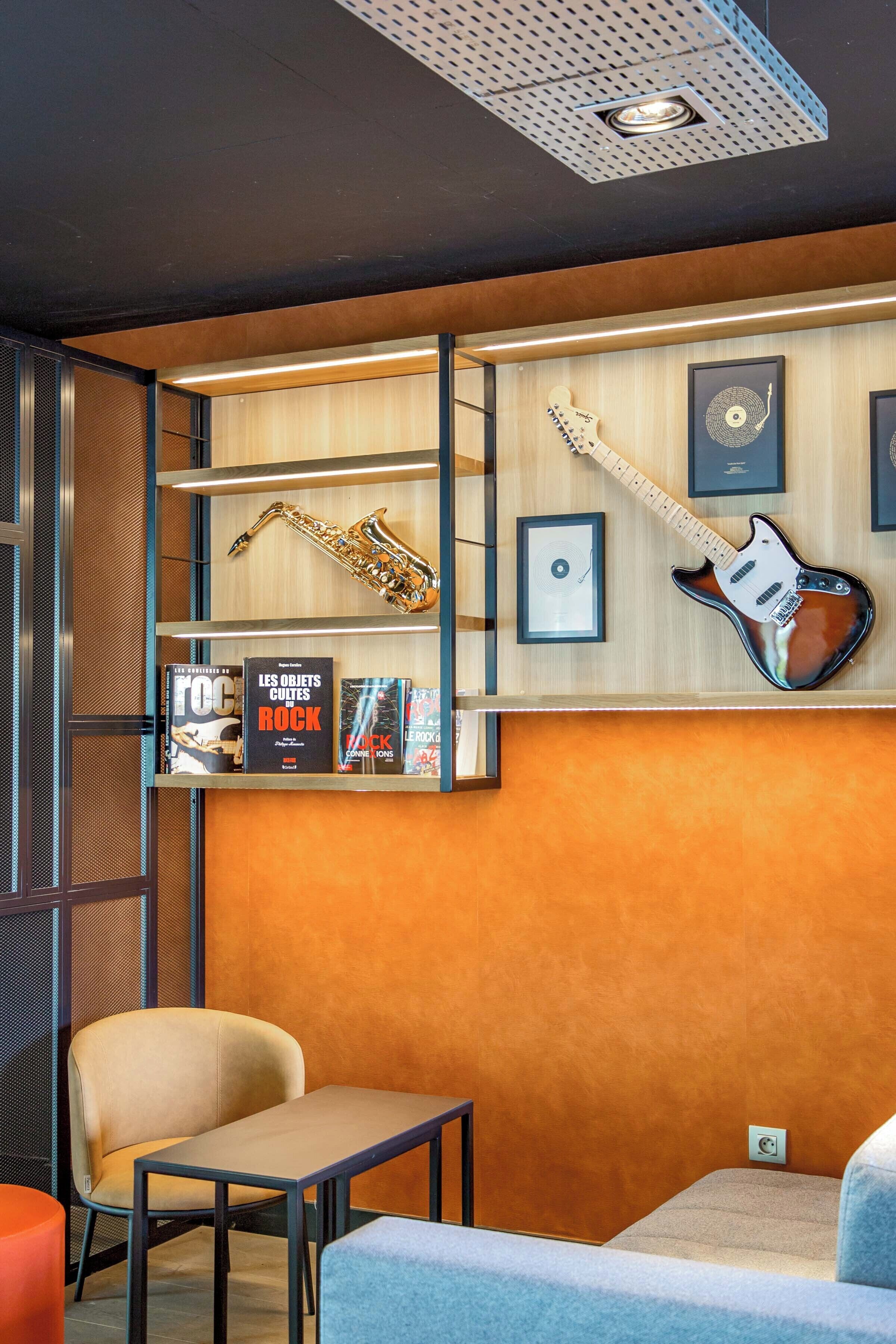 Une pièce avec un mur en bois, un saxophone, une guitare, des livres encadrés et une chaise.