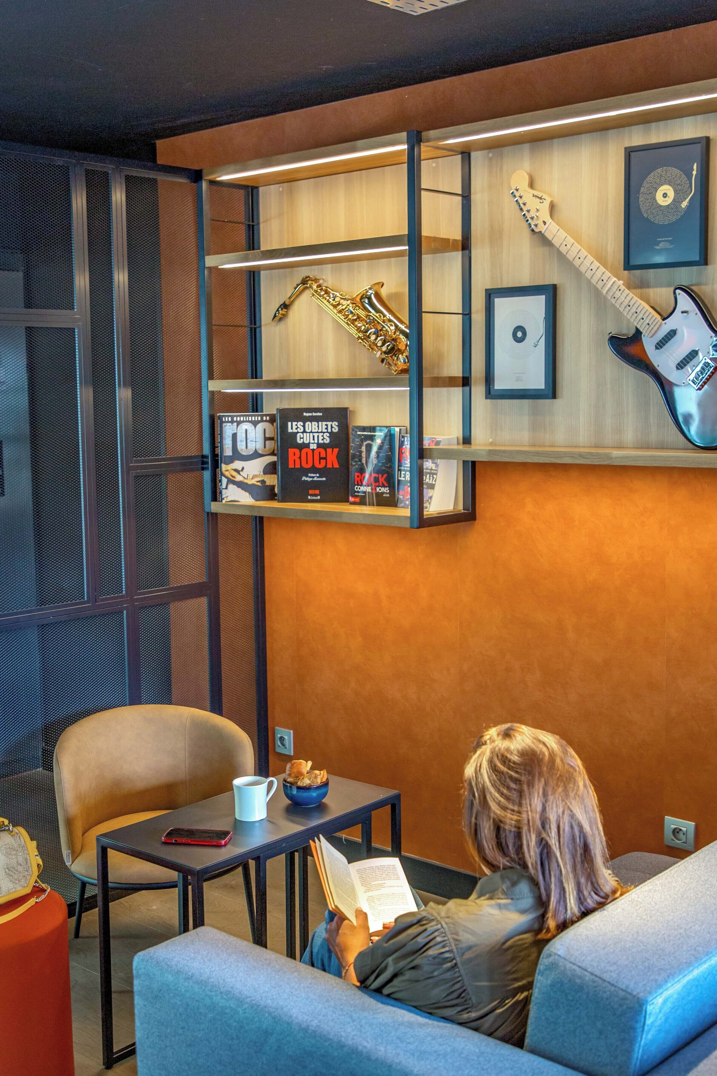 Une pièce moderne comprenant un canapé, une table avec une tasse de café, une bibliothèque remplie de livres et une guitare, ainsi qu’un saxophone.