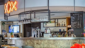Un espace bar avec un panneau lumineux au néon, des tabourets de bar et un tableau affichant le menu.