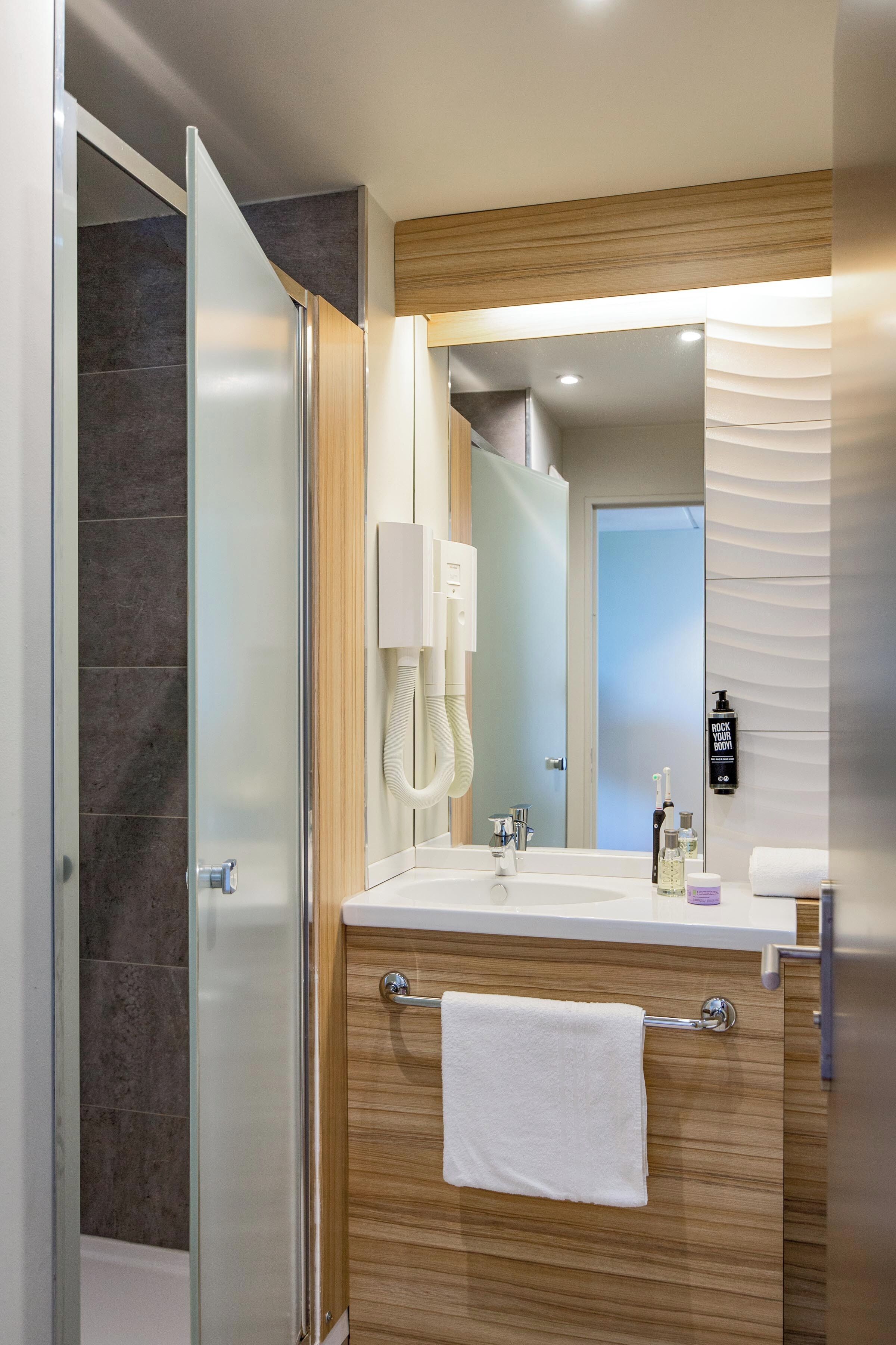 Une salle de bain moderne avec une douche à parois de verre, un meuble-lavabo en bois, un grand miroir et un porte-serviettes.