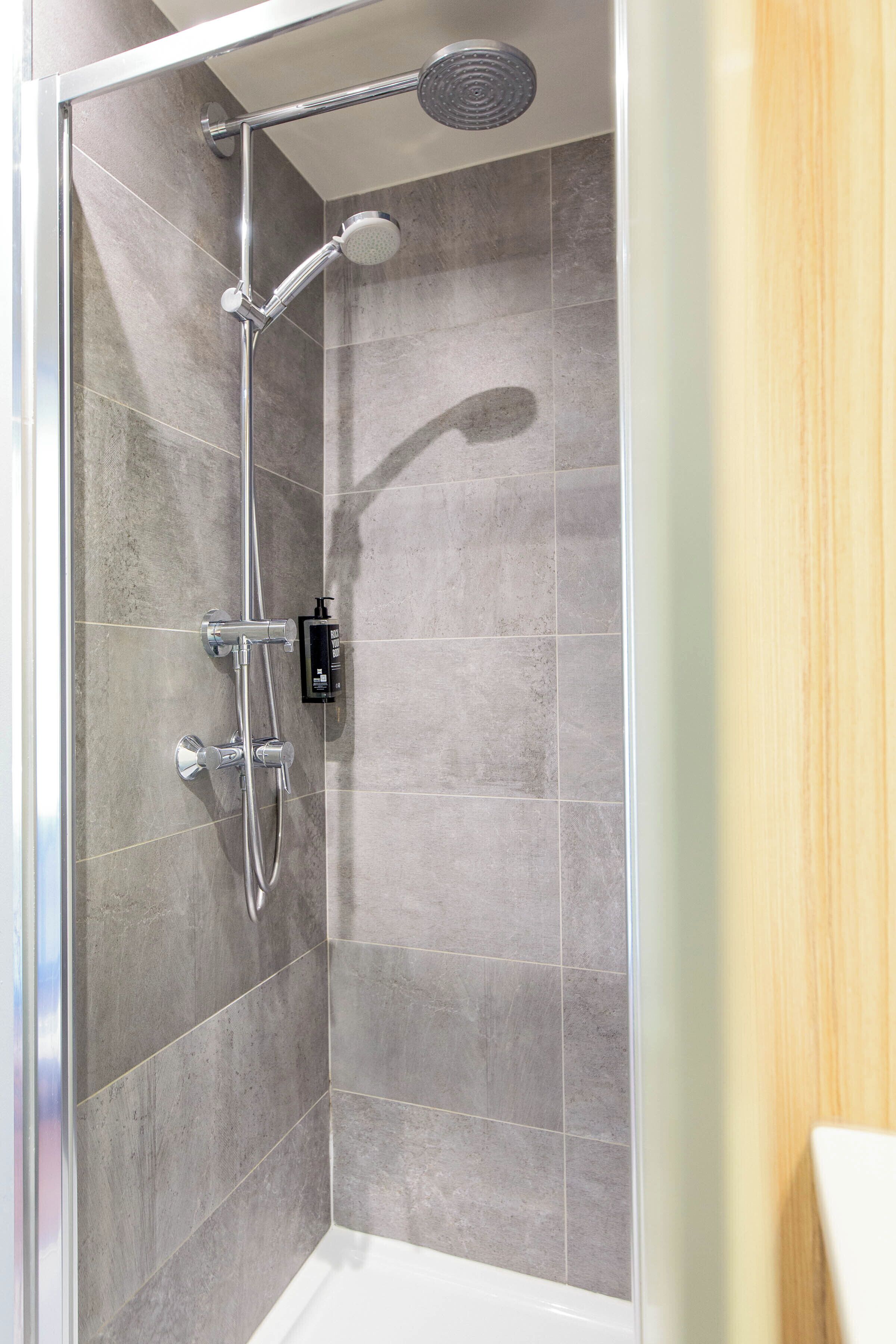 A shower with a handheld showerhead, a wall-mounted faucet, and a control panel.