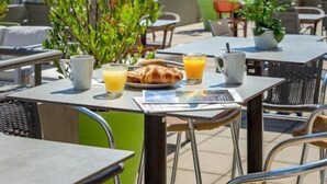 Un espace extérieur aménagé pour les repas, avec des tables, des chaises et un bâtiment en arrière-plan.