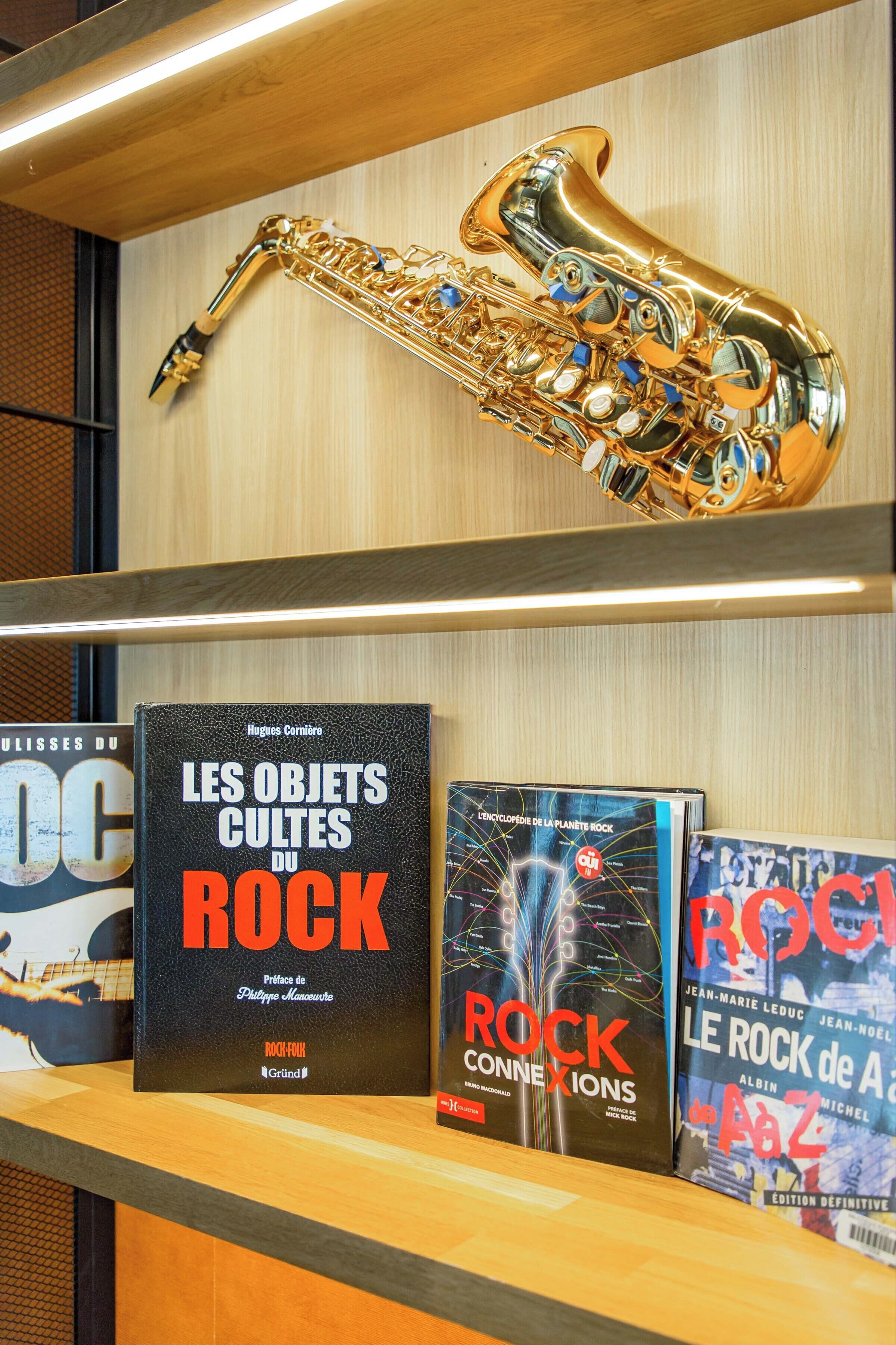 Un saxofón sobre una estantería con tres libros titulados 'Les Objets Cultes du Rock', 'Rock Connexions' y 'Le Rock de A'.