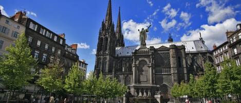A historic cathedral with a central fountain and statues, surrounded by trees and buildings.