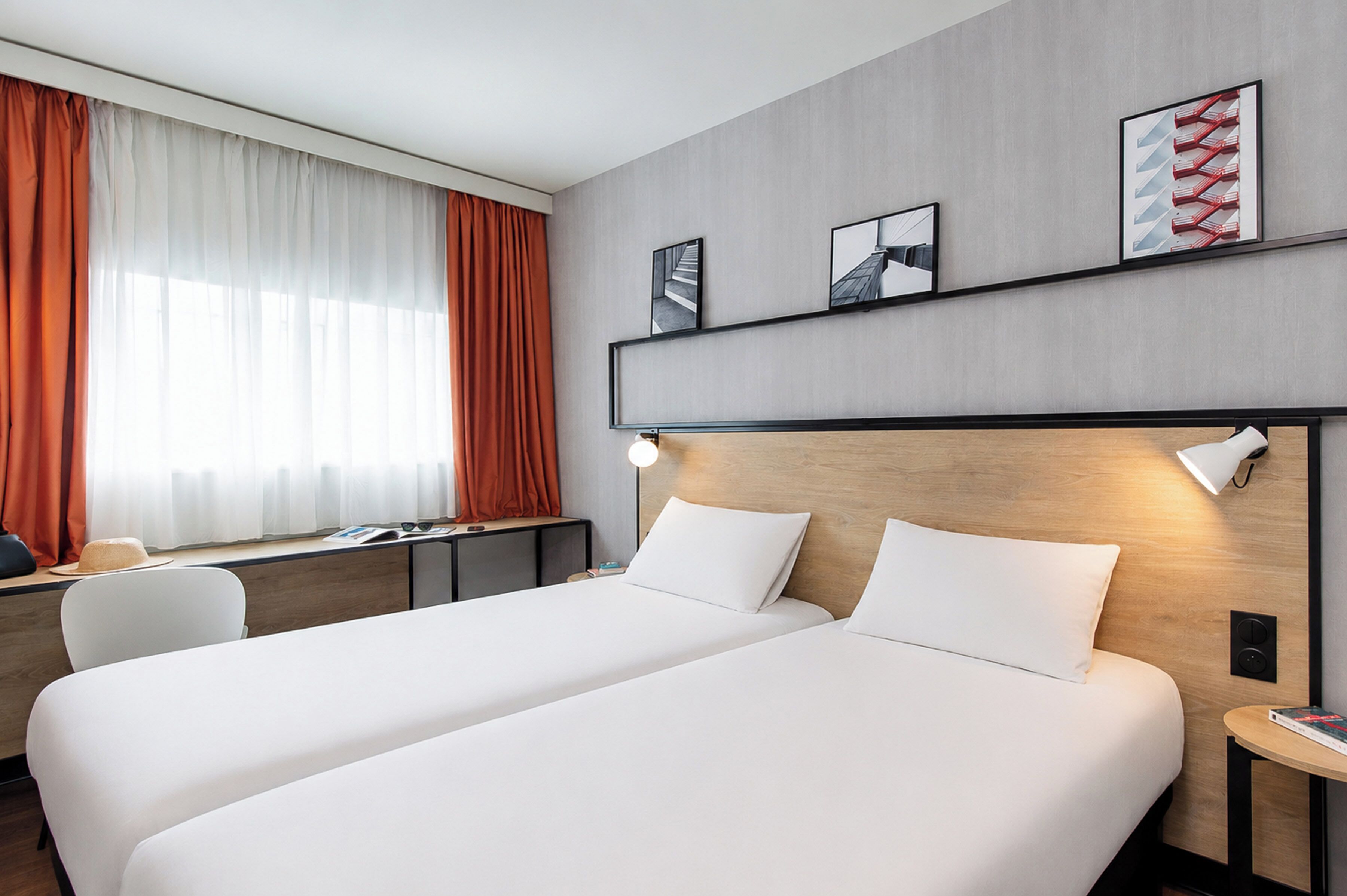 A hotel room with two beds, a desk, a chair, and a window with curtains.