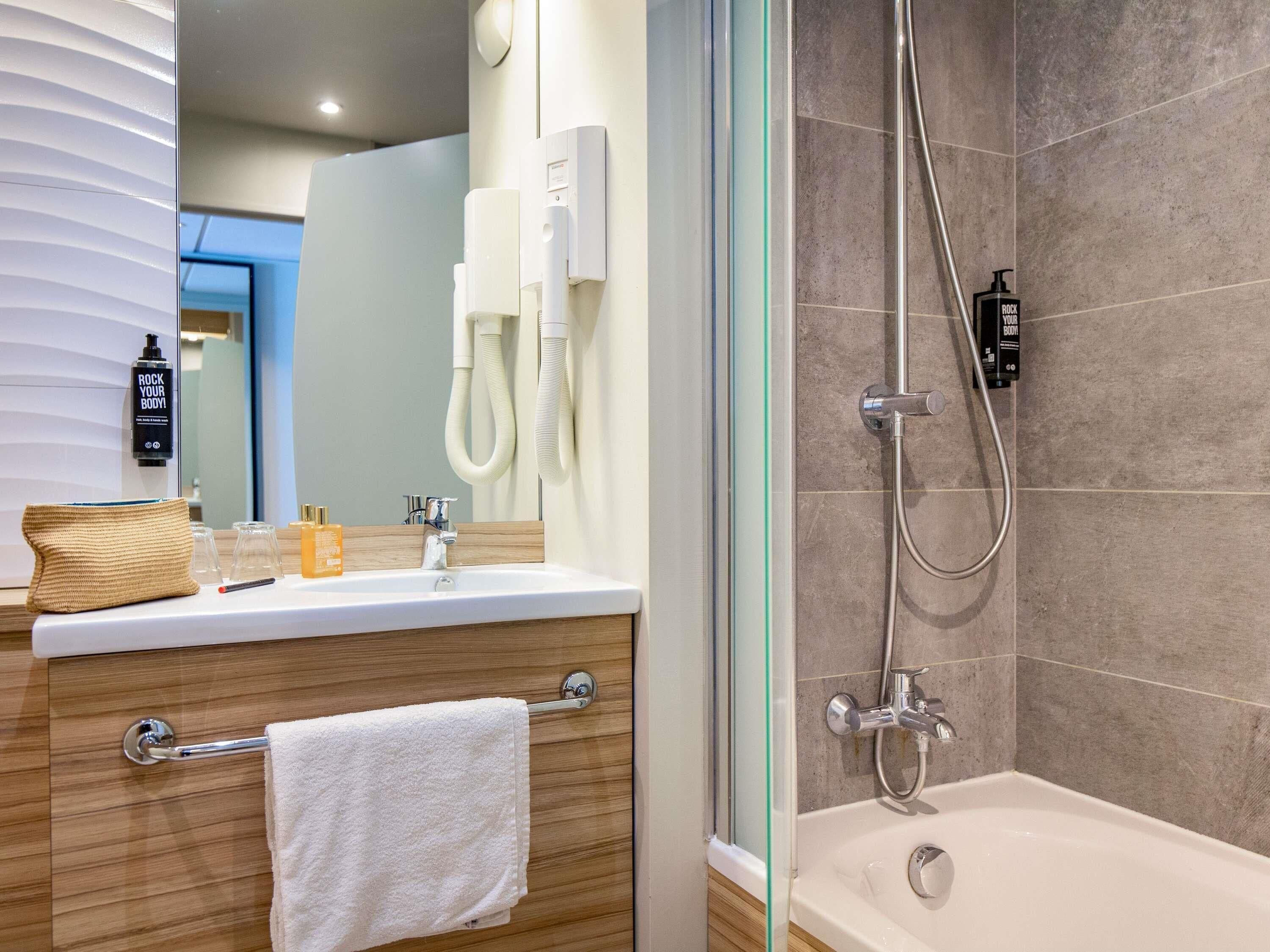 Un baño con ducha, lavamanos y un perchero para toallas.