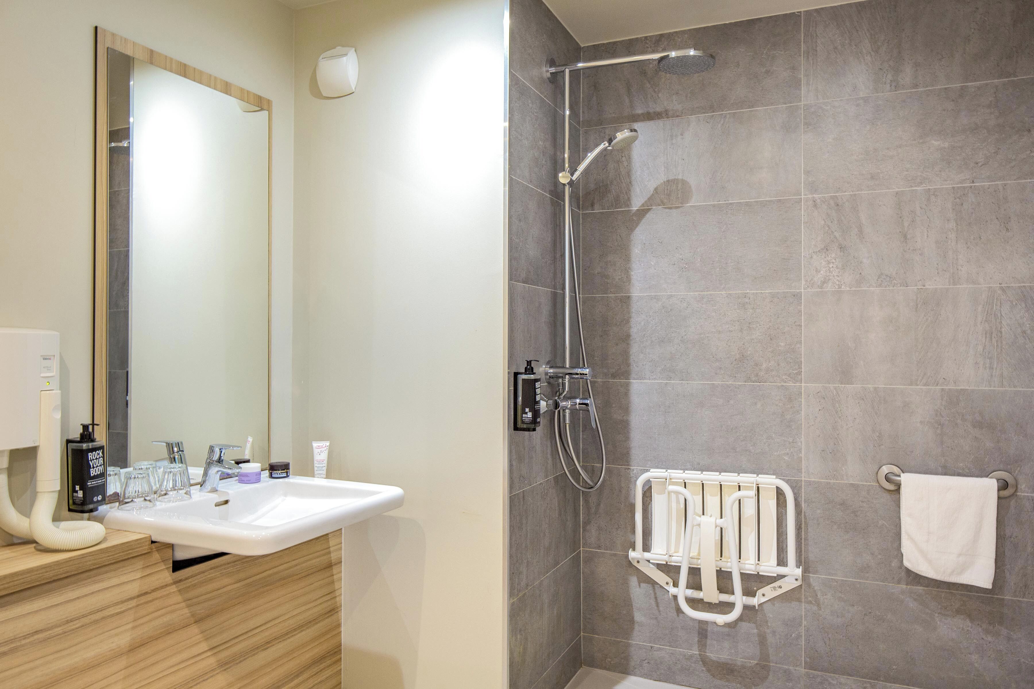 Une salle de bain équipée d’un lavabo, d’un miroir, d’une douche et d’un porte-serviettes.