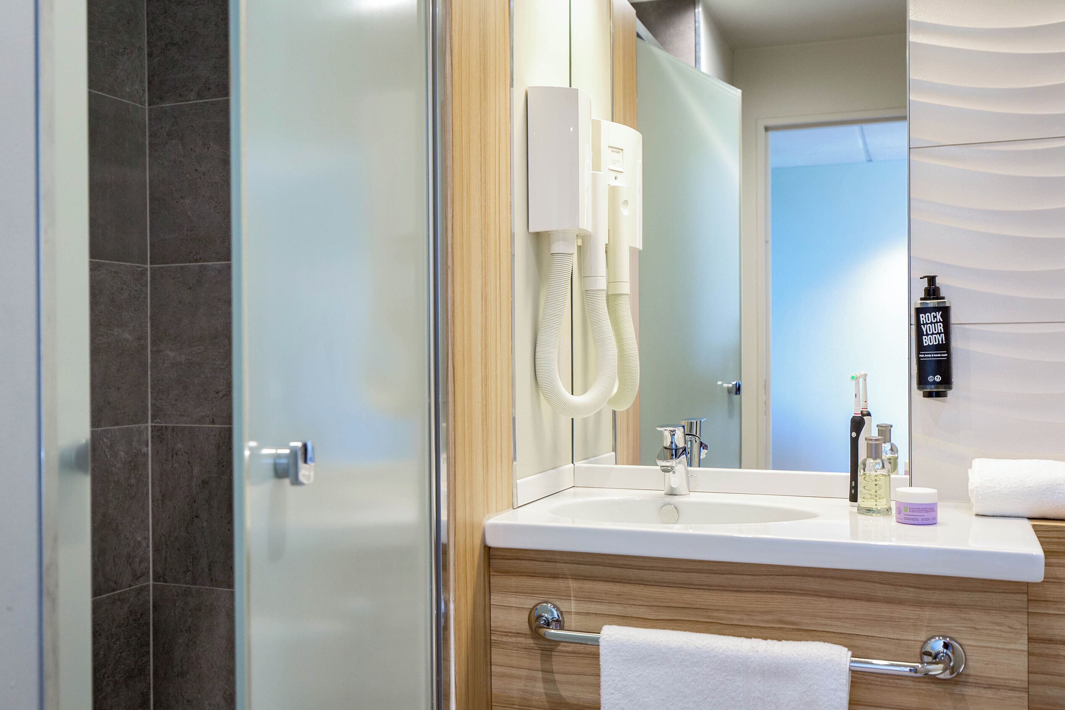 A modern bathroom with a glass shower enclosure, a white sink with a mirror, and a towel rack.