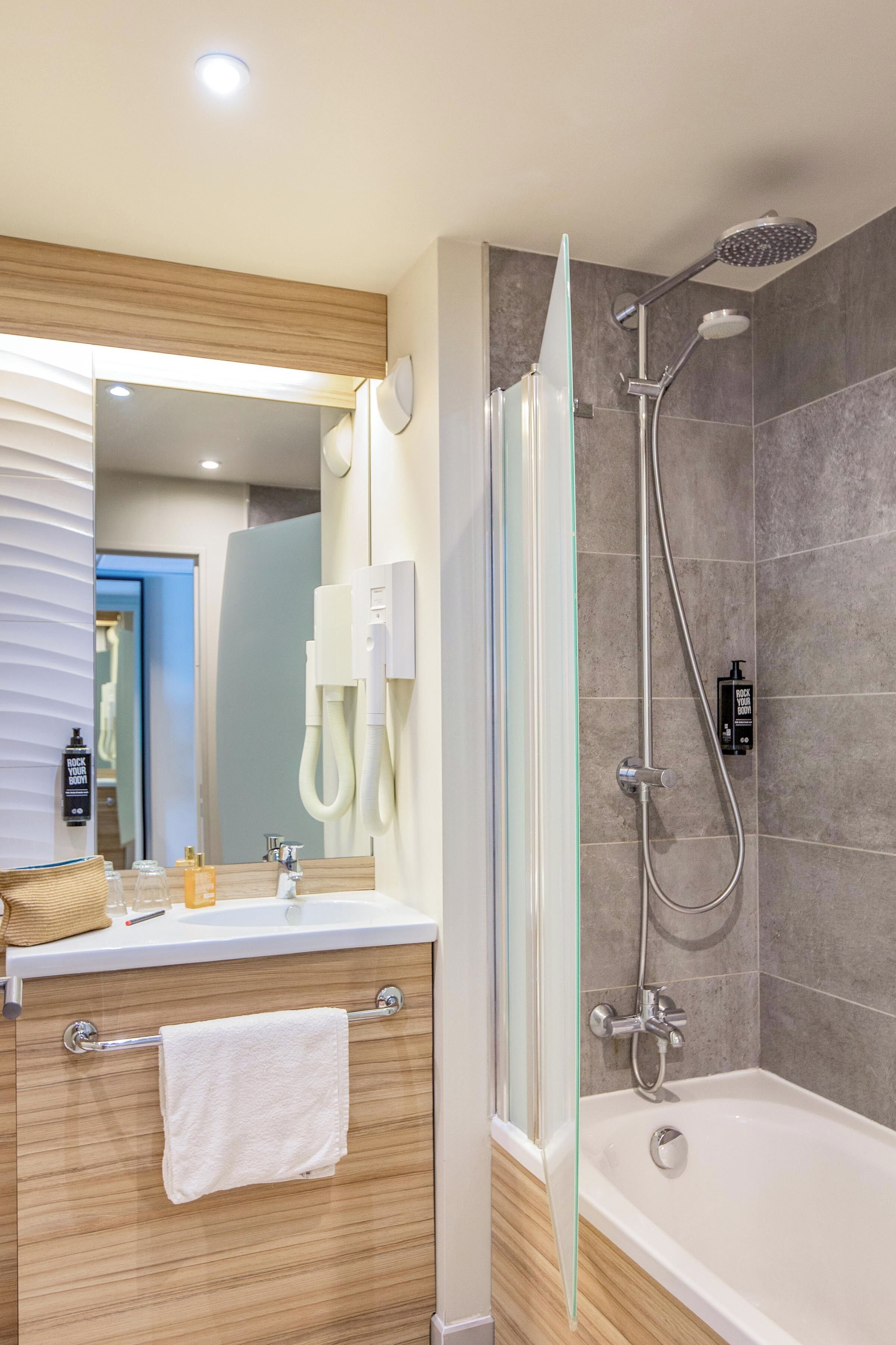 A modern bathroom with a glass shower enclosure, a bathtub, a vanity with a towel rack, and a mirror.