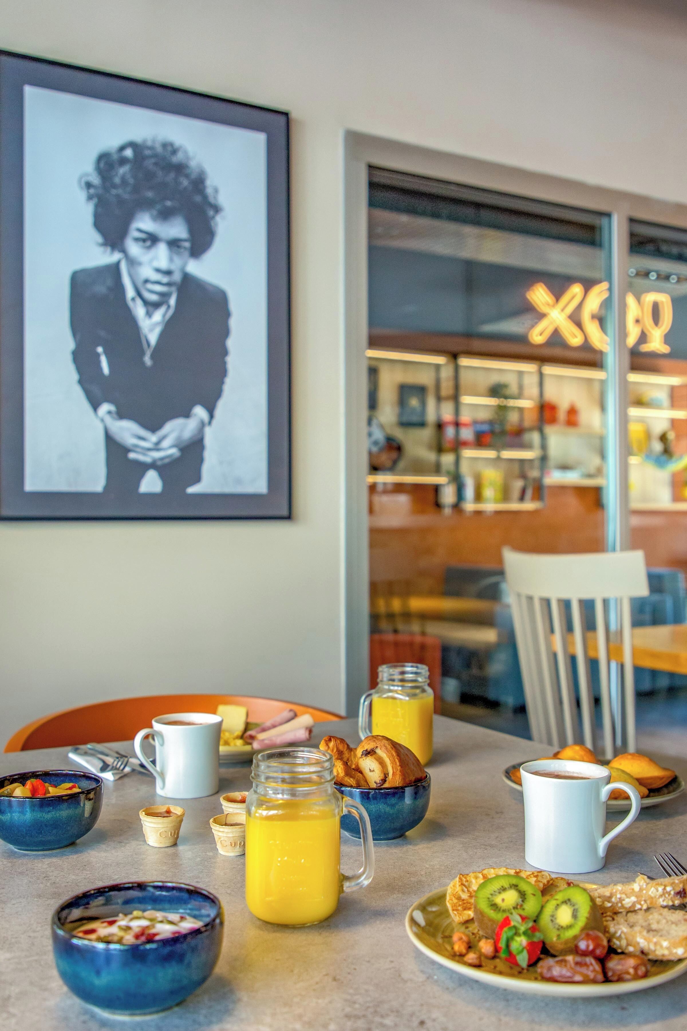 A breakfast table with various dishes, a framed picture on the wall, and a café in the background.