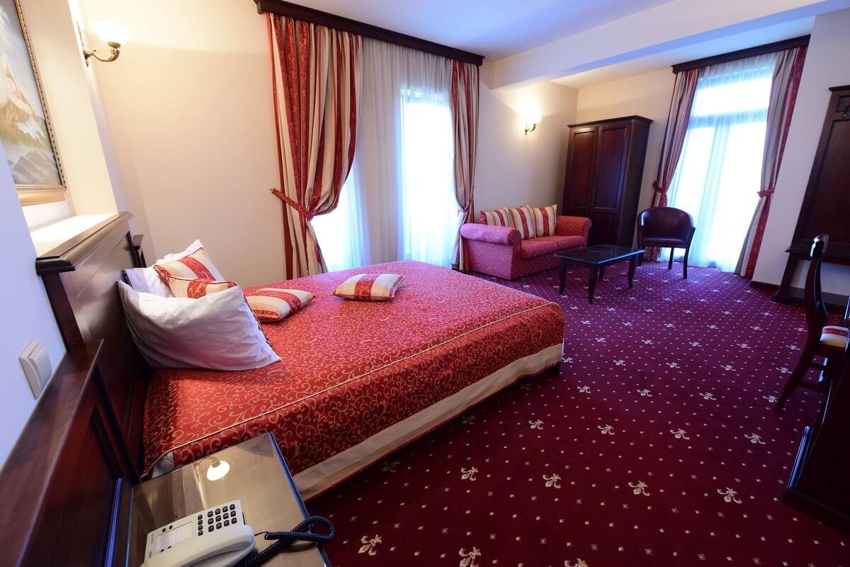 Hotellihuone, jossa on suuri sänky, kirjoituspöytä, jossa on puhelin, tuoli ja sohva.