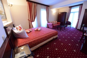 A hotel room with a large bed, a desk with a telephone, a chair, and a sofa.