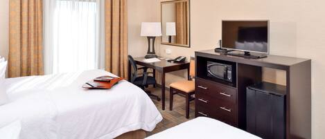 A hotel room with two beds, a desk with a chair, a TV, a microwave, and a small refrigerator.