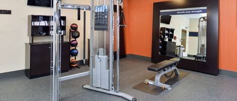 Une salle de sport équipée d’un support à squats, d’un banc et de divers poids.