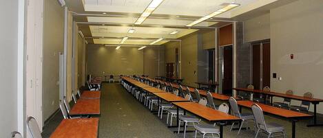 Un salón de conferencias con largas mesas y sillas, equipado con luces en el techo y suelo alfombrado.