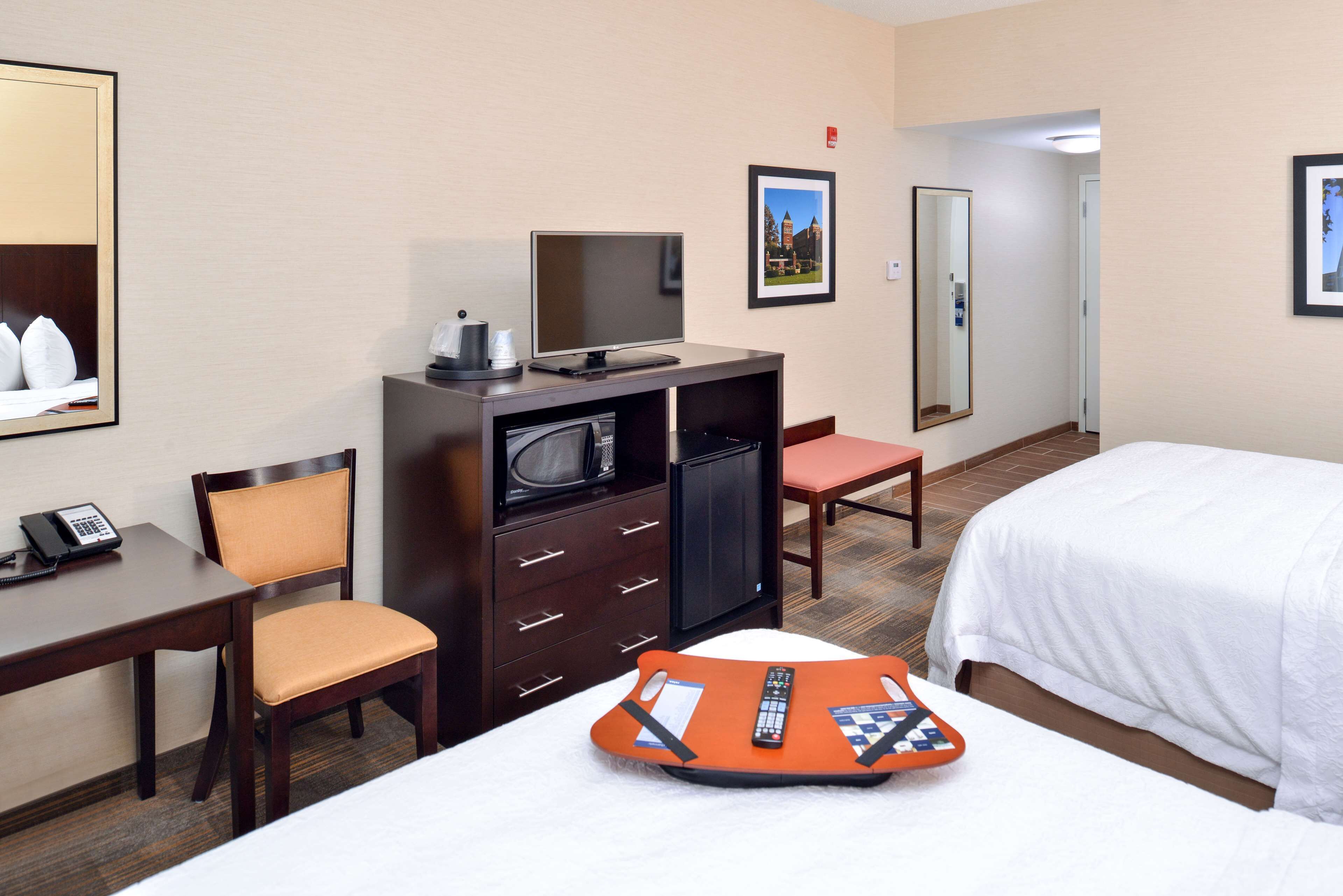 A hotel room with a bed, a desk with a telephone, a chair, a television, and a small table with a remote control and a book.