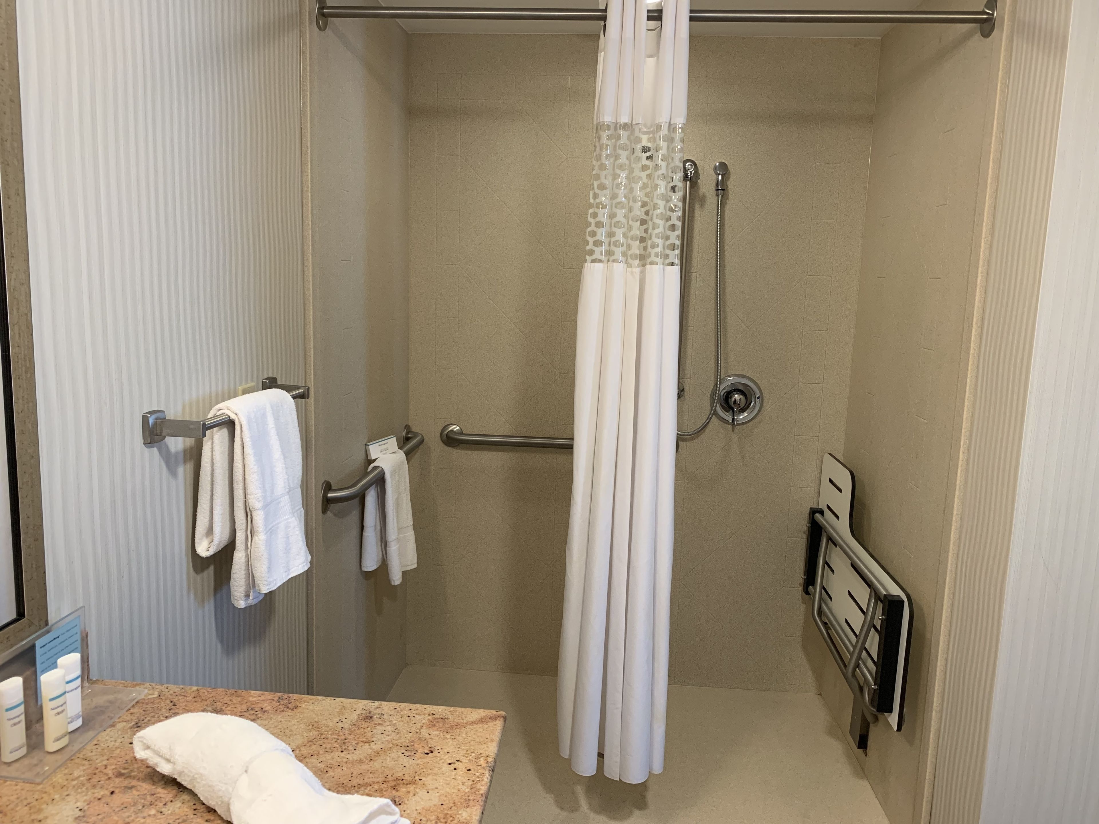 A shower with a handheld showerhead, a towel rack with towels, and a shower curtain.
