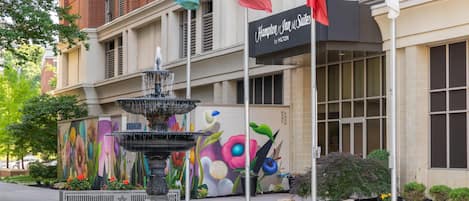 A hotel with a fountain, a mural, and multiple flags.