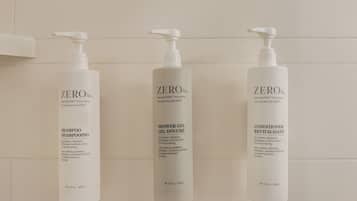 Three bottles of ZERO% shampoo, shower gel, and conditioner on a white tiled wall.