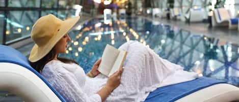 Una persona recostada en una silla de descanso leyendo un libro en un ambiente moderno con piso de vidrio e iluminación decorativa.