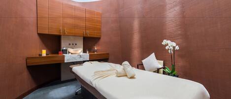 A modern spa room with a curved ceiling, a massage table, wooden cabinets, and a potted orchid.