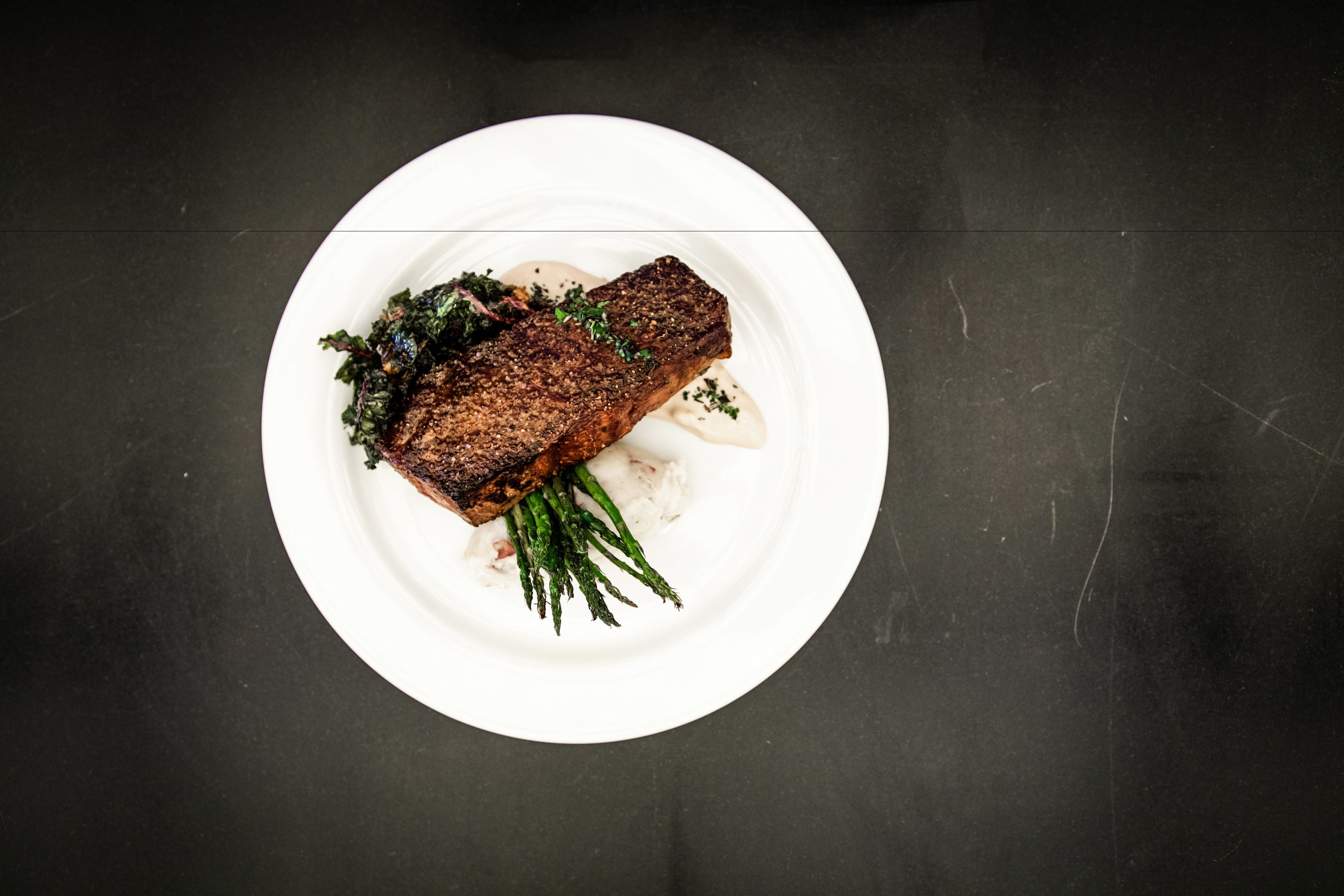 Un plato blanco con un filete de carne, espárragos y salsa cremosa.