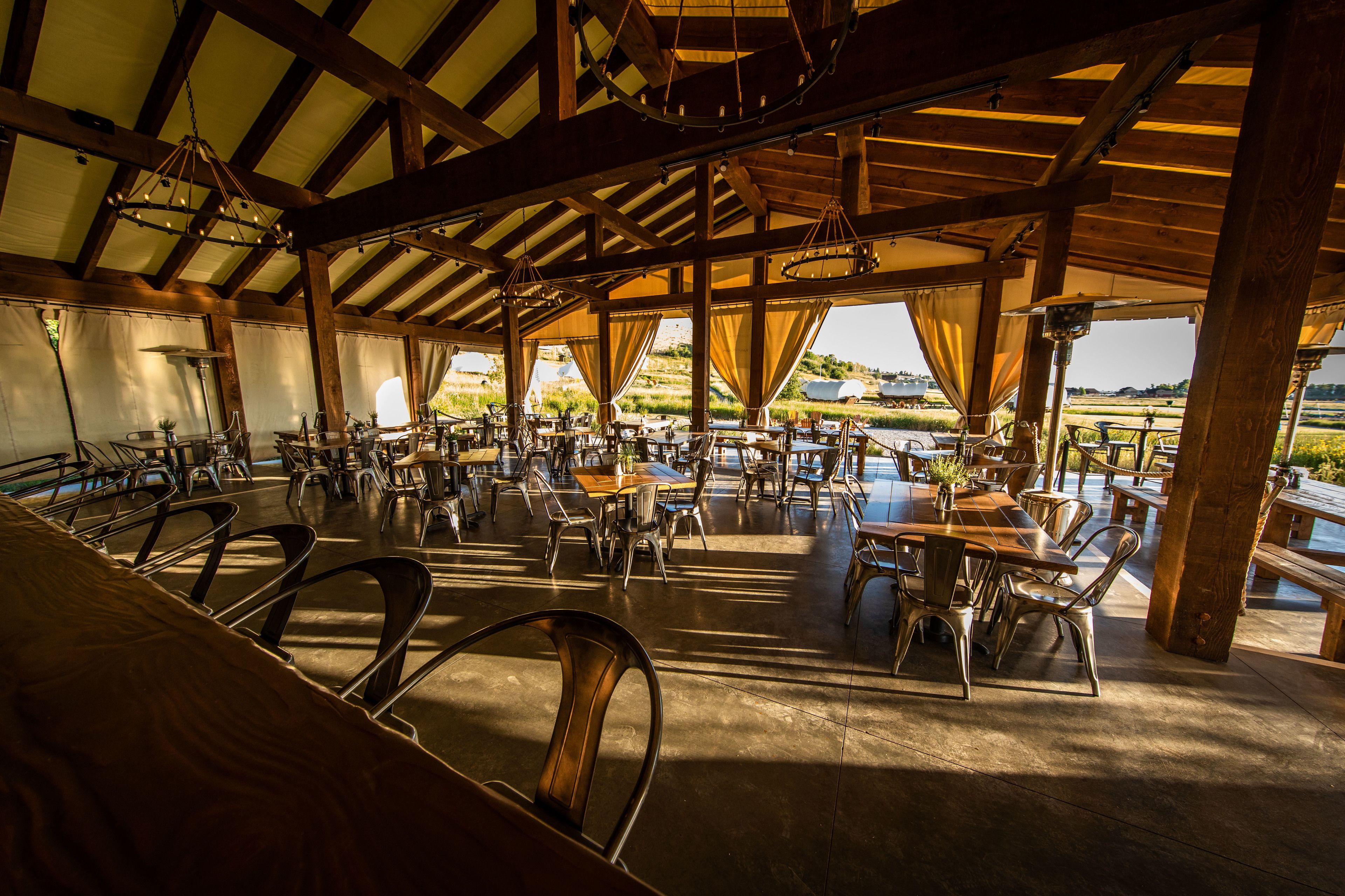 An outdoor dining area with multiple tables and chairs, wooden beams, and a view of the landscape.