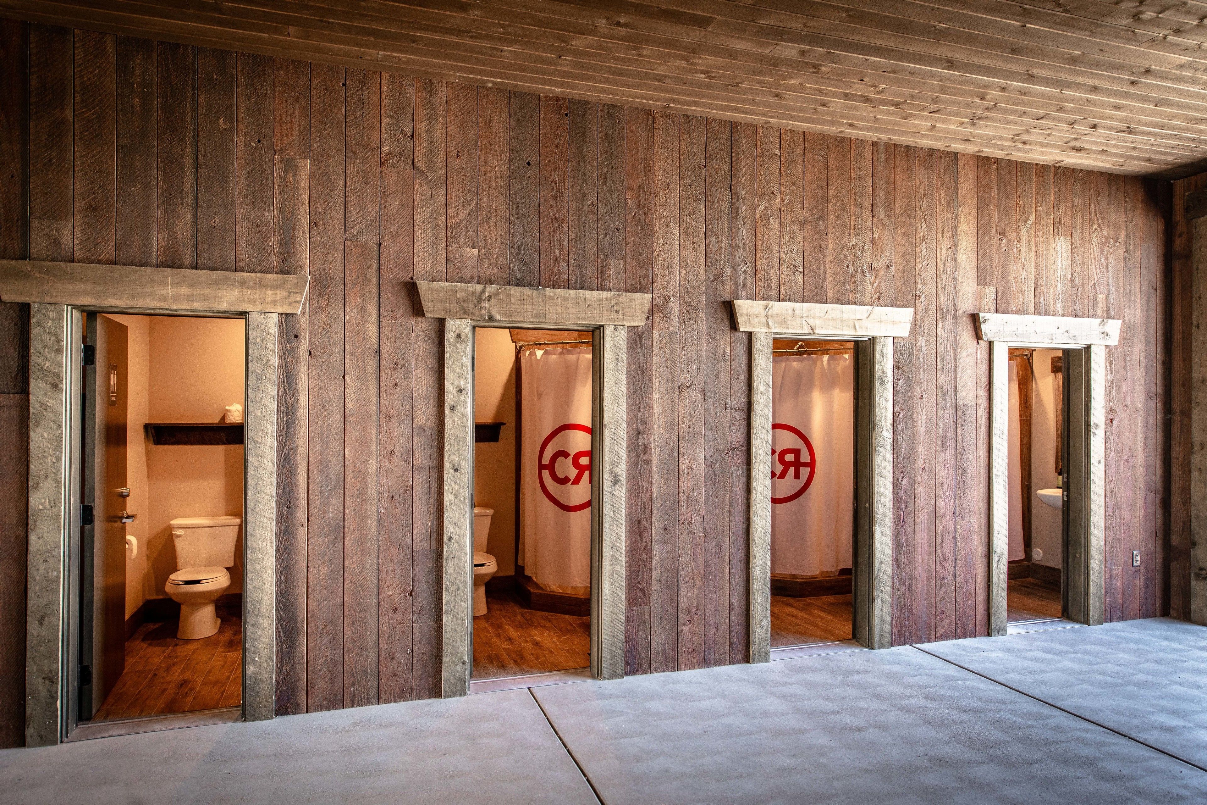 Interior de madera con varios accesos a baños, cada uno con inodoro y cortina de ducha visibles.