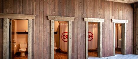 Interior de madera con varios accesos a baños, cada uno con inodoro y cortina de ducha visibles.
