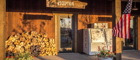 A wooden building with a reception sign, stacked firewood, a refrigerator with 'ICE' sign, and an American flag.