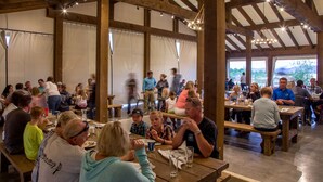 A spacious dining area with wooden beams and tables, large windows, and a view of the outdoors. - Conestoga Ranch (Garden City)