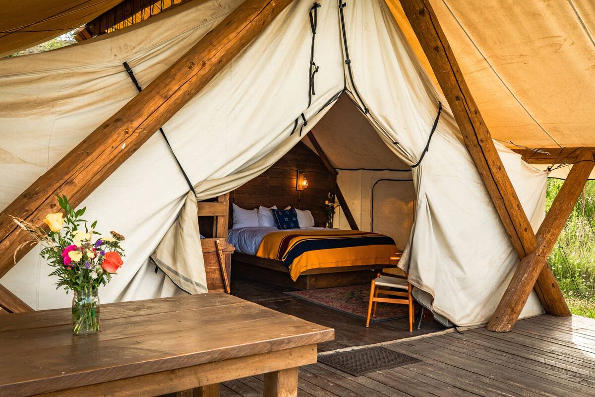 A tented accommodation with a bed, a wooden table, and a vase of flowers.