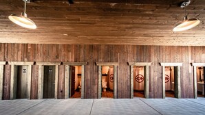 A wooden interior with multiple doorways leading to individual rooms, a concrete floor, and hanging pendant lights. - Conestoga Ranch (Garden City)