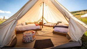 A spacious tent with two beds, a small table, and a colorful ottoman. - Conestoga Ranch (Garden City)