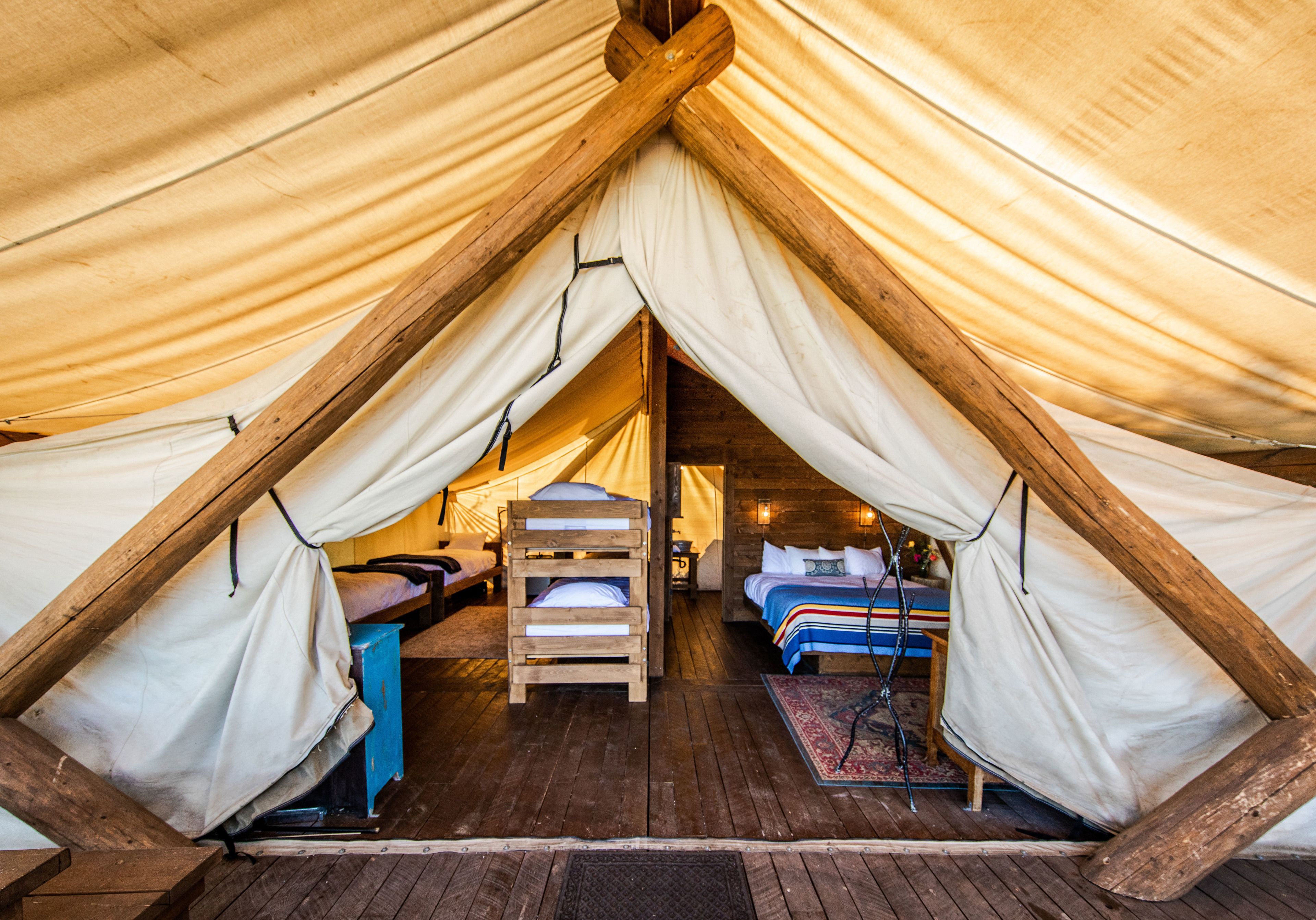 Eine Zelthotelunterkunft mit zwei Schlafbereichen, Holzboden und einer zentralen Sitzecke.