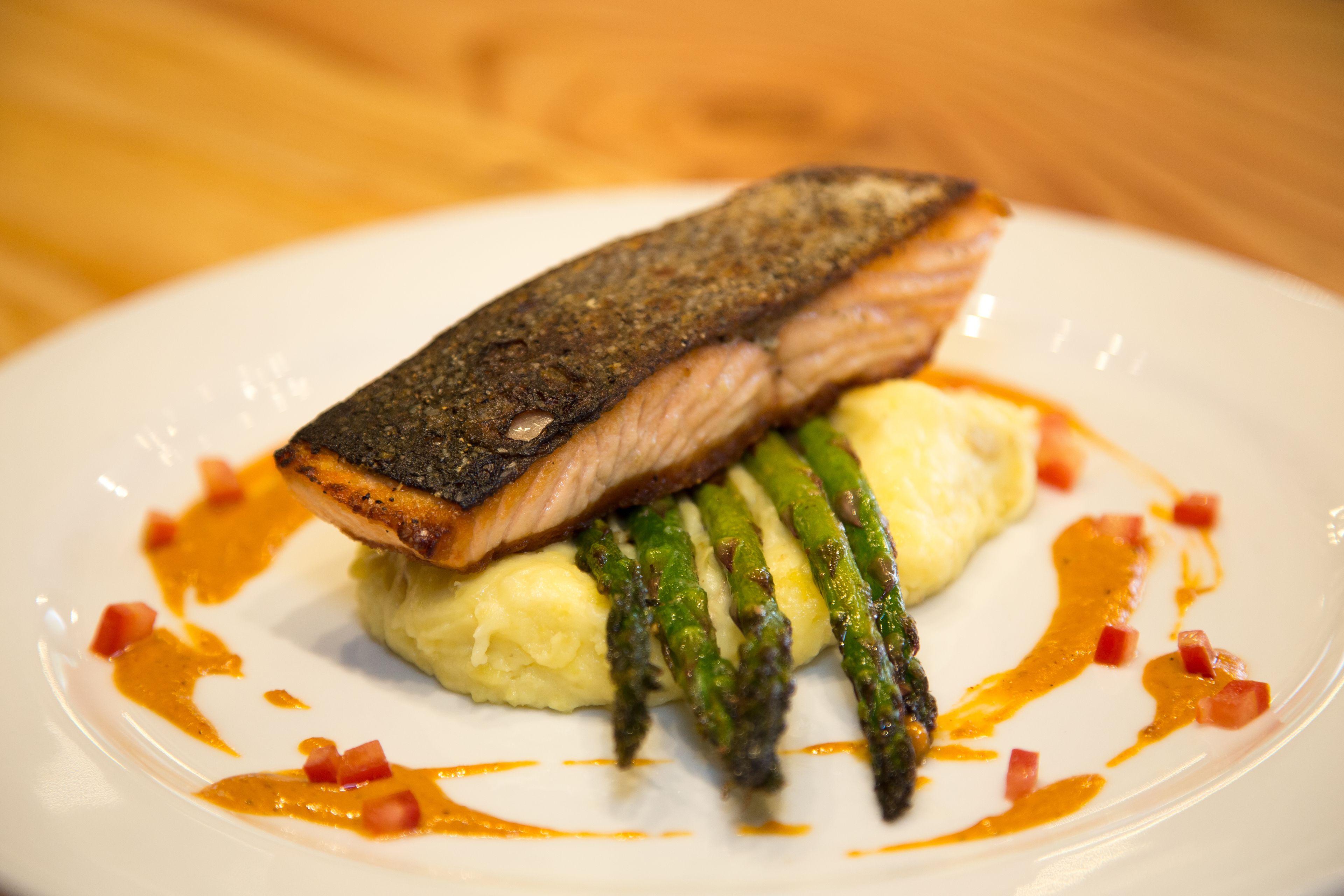 A plate with a piece of salmon, asparagus, and mashed potatoes.