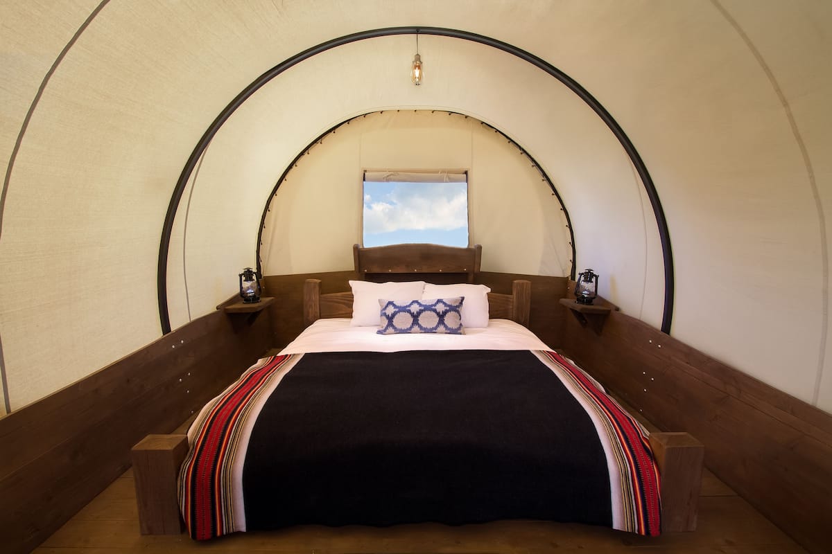 A tent-style room with a bed, wooden headboard, and two bedside tables with lamps.