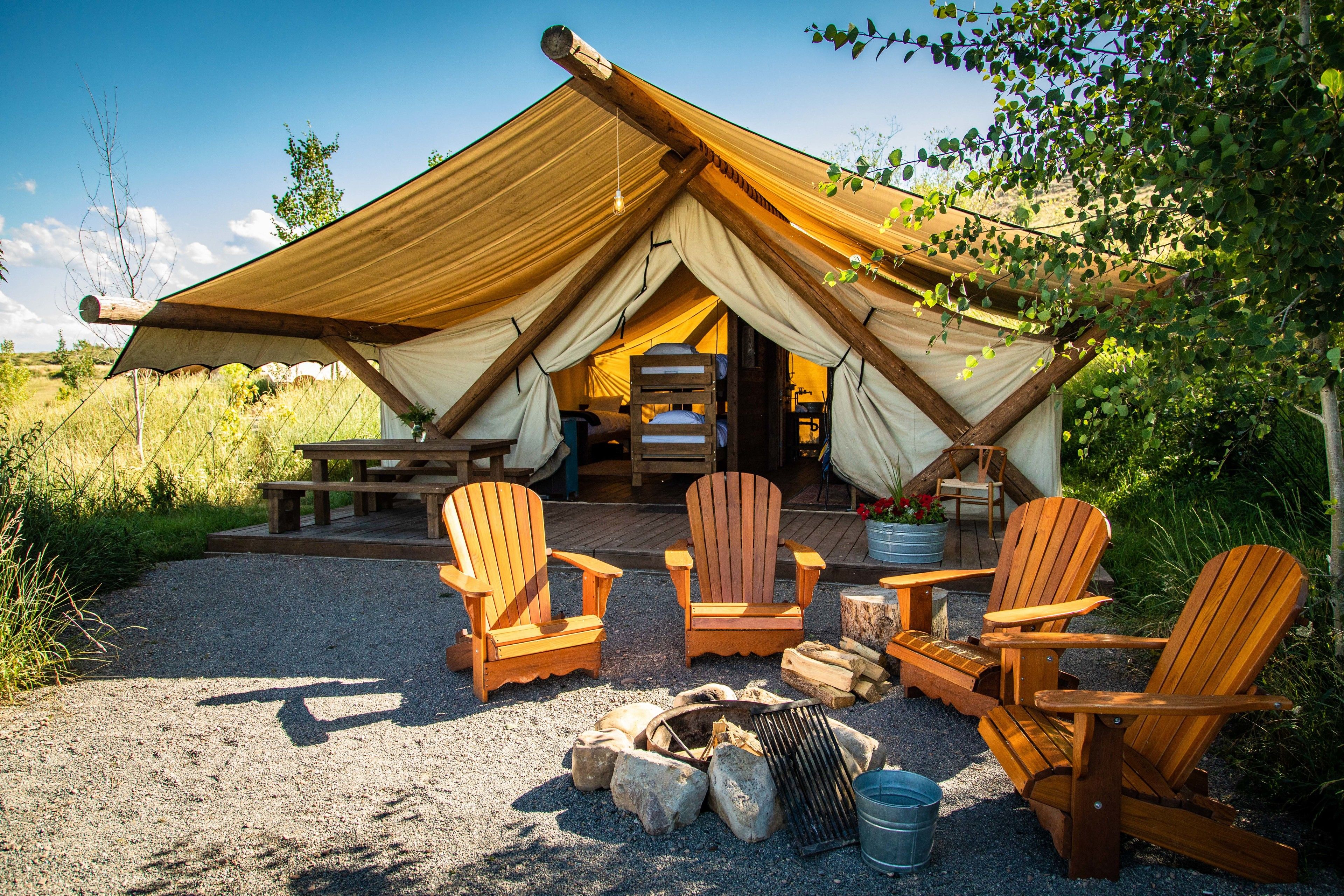 A tent with a wooden deck, four Adirondack chairs, a fire pit, and a picnic table.