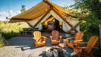 A tent with a wooden deck, four Adirondack chairs, a fire pit, and a picnic table.