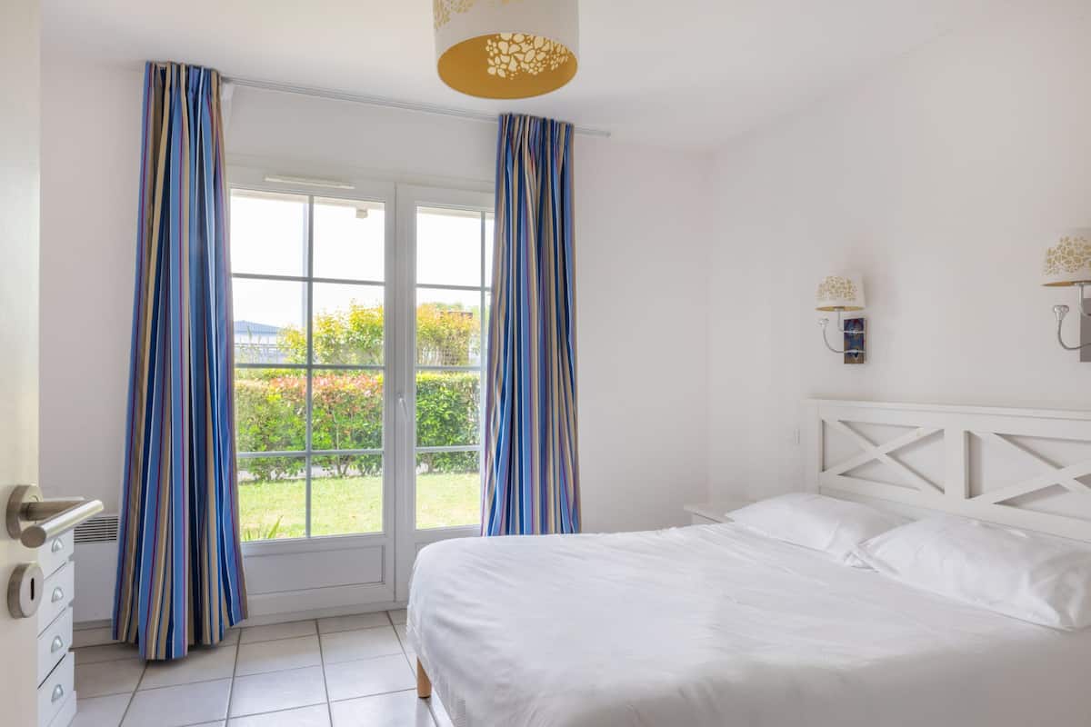 Une chambre à coucher avec un lit, des rideaux, une fenêtre et une porte.