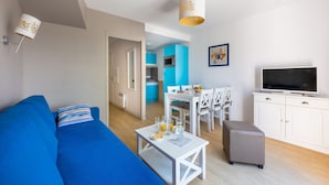 Una sala de estar moderna con un sofá azul, una mesa de centro blanca y un televisor sobre un mueble blanco.